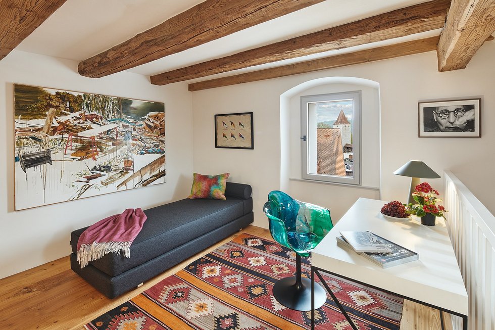 Gemütliches Zimmer im Engelwirt Hotel & Apartments in Berching im Altmühltal mit offenliegenden Deckenbalken, grauem Sofa, Tisch mit stylischem Drehstuhl und mehreren Bildern an der Wand